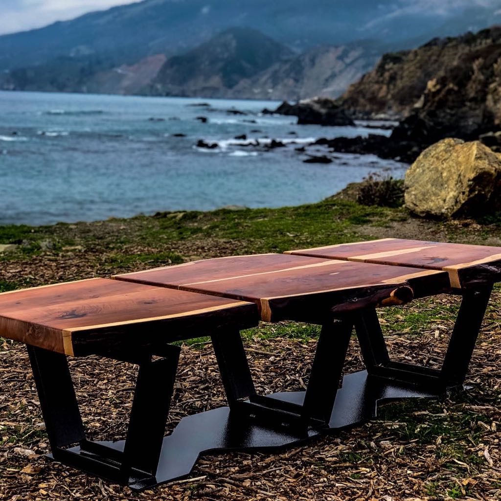 Live edge tables on black steel bases, set out on a bluff above the ocean