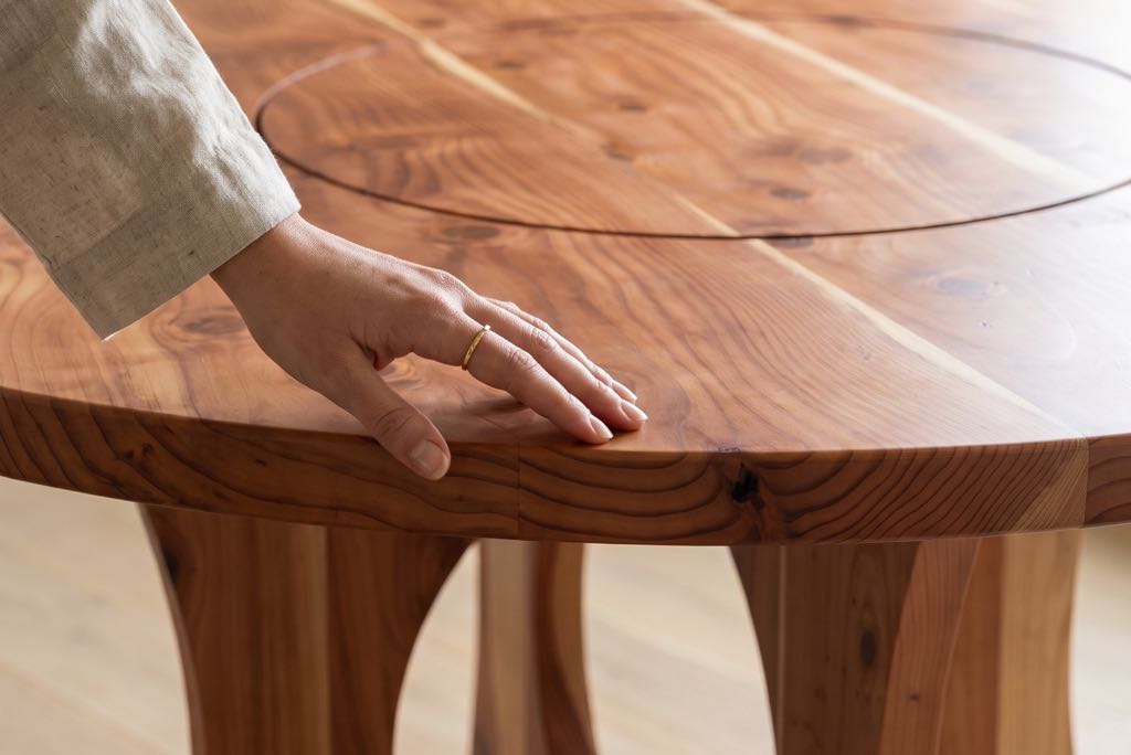 A hand resting on the edge of the redwood top beside a sapwood stripe