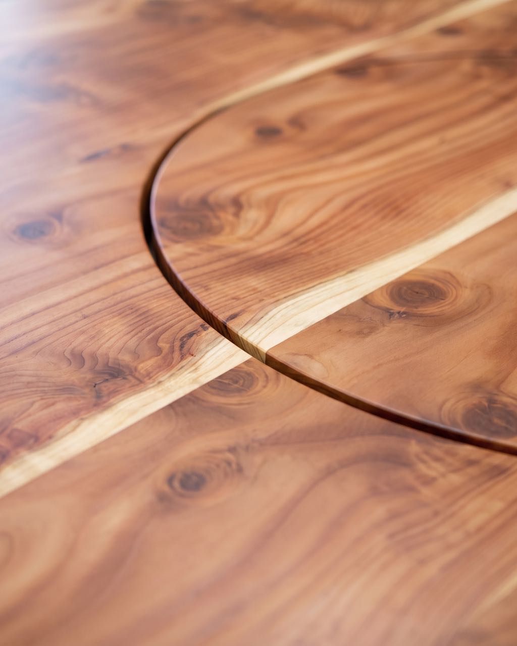 Close-up of the redwood top where the lazy Susan's routed circle cuts across a pale sapwood stripe and the grain carries on across the seam