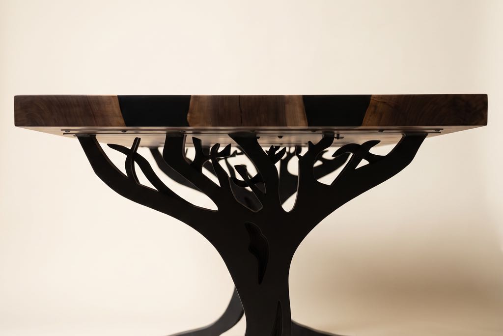 The end of the table straight on: the walnut end grain with its black-filled checks, above the branches of one steel leg