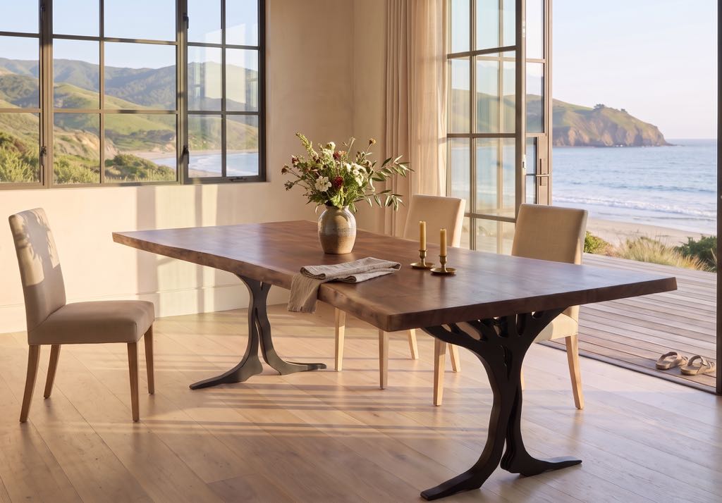 The tree-leg table with a vase of wildflowers in a styled dining room with windows onto green hills and the ocean