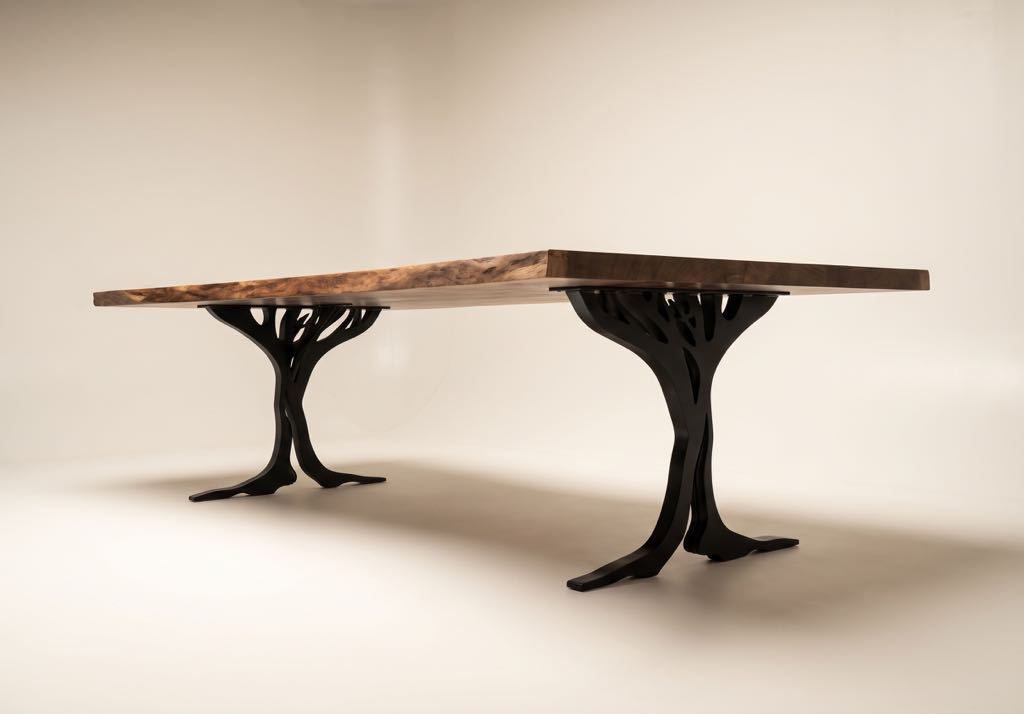 The claro walnut tree-leg table in a three-quarter view on a cream studio backdrop, both steel legs in view