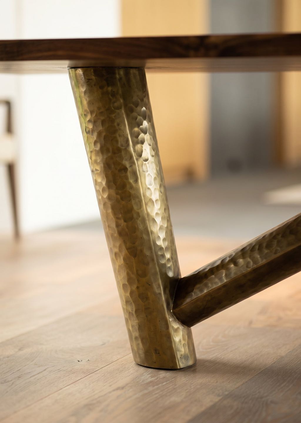 Close-up of a hand-hammered metal leg of the orchard walnut table, with the diagonal strut meeting it near the floor