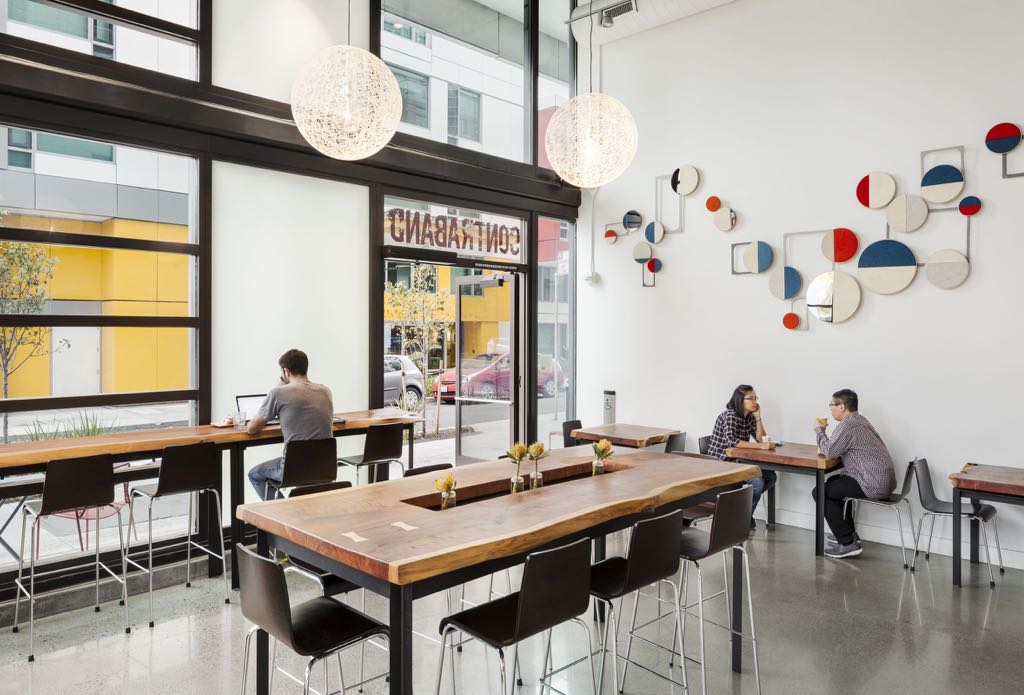 Inside the former Contraband Coffee in San Francisco: redwood café tables for two along a white wall, with a long live-edge redwood table and a window counter in front