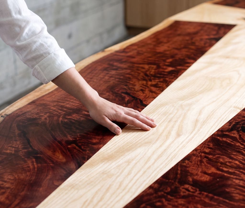 A hand on the conference top, where a band of pale ash meets dark curly redwood