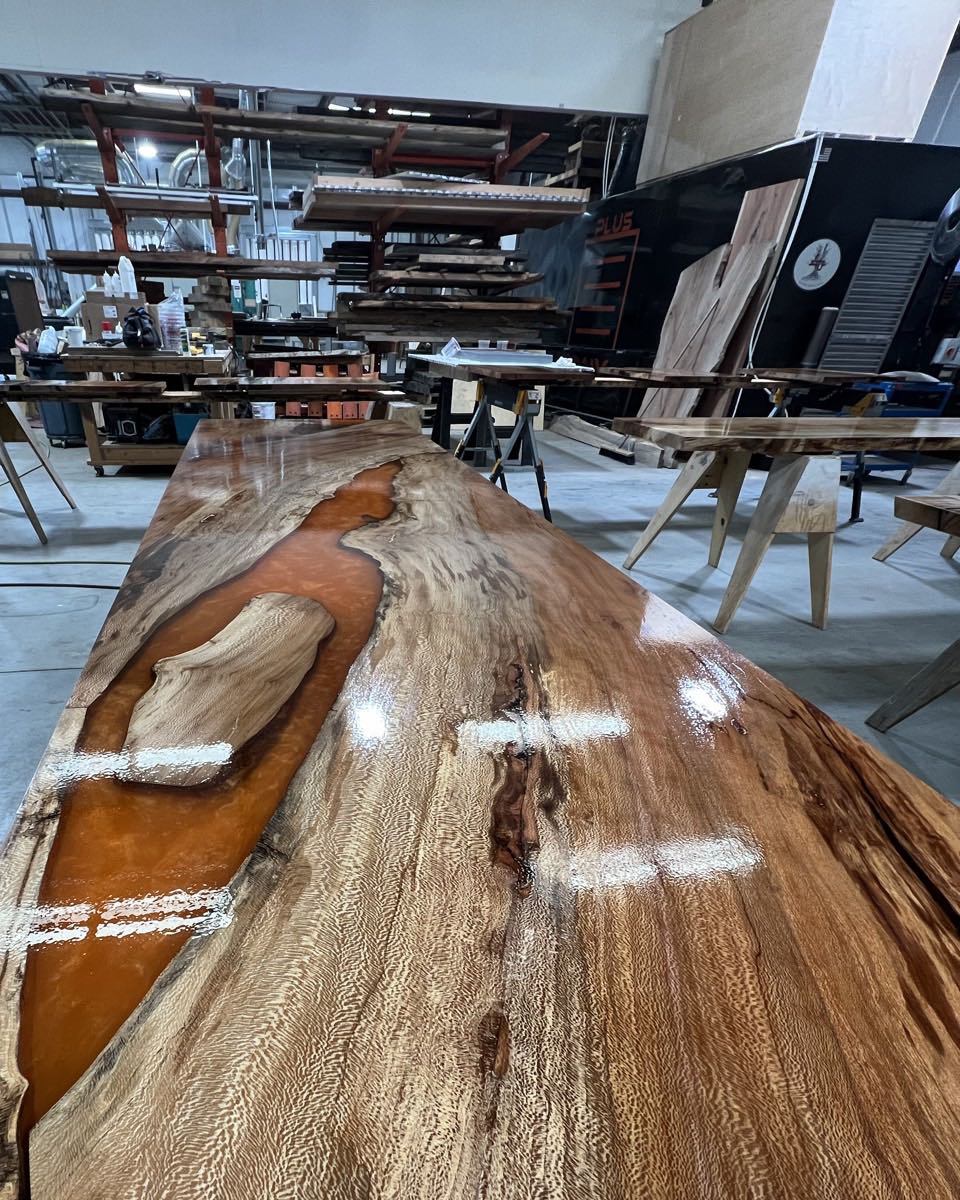 The slab for the front of the bar, lying flat in our shop with the orange resin river poured around a pale island of wood, and the lace-like grain running down the slab