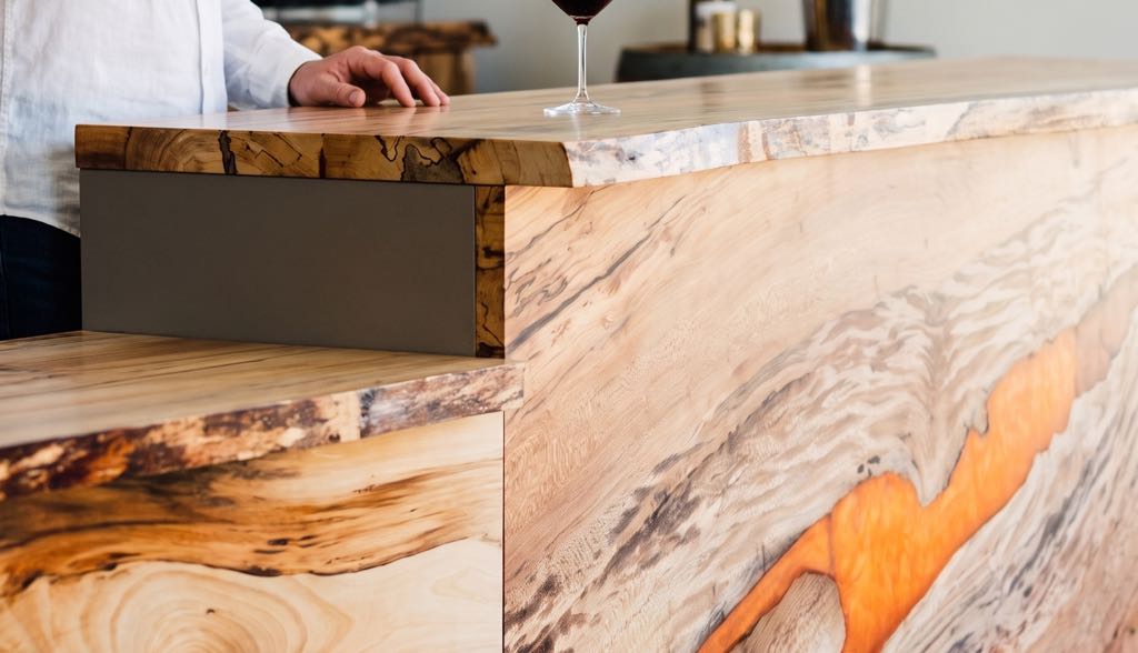 A glass of red wine being poured on the live-edge sycamore top